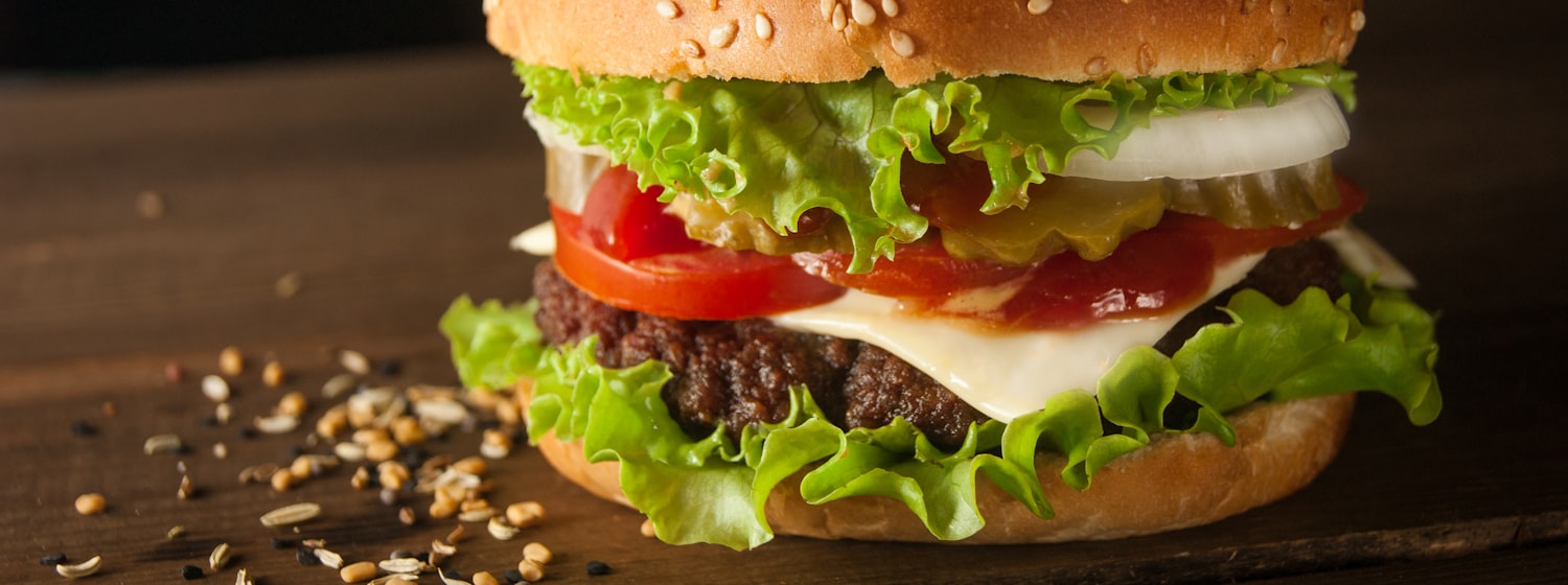 A beef burger with melted cheese beside a glass of red wine