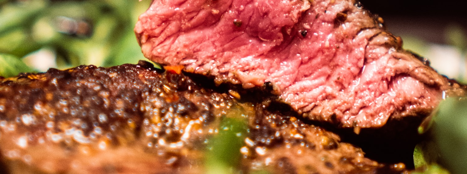 A grilled ribeye steak resting on a board beside a glass of red wine
