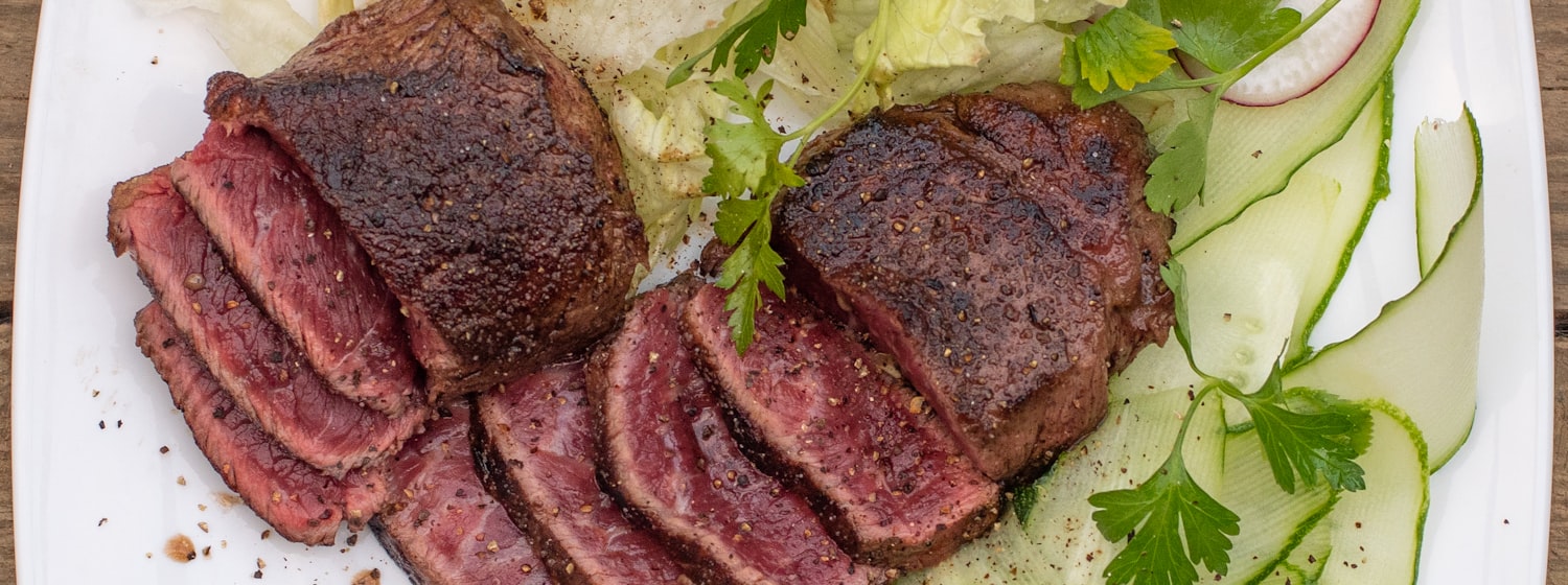 Sliced roast venison on a plate beside a glass of red wine